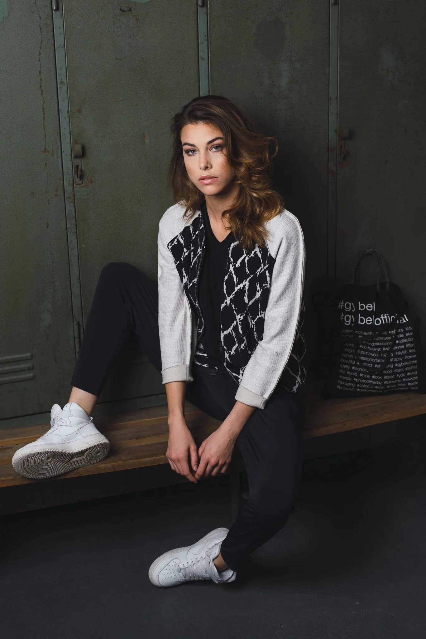 Casual portrait of a woman sitting on a bench in front of green metal lockers.